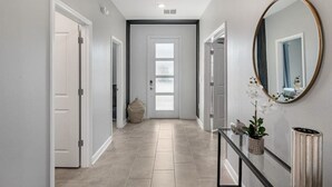 Un couloir au design moderne, avec une porte en verre au bout, un miroir sur le mur et une petite plante posée sur une console.