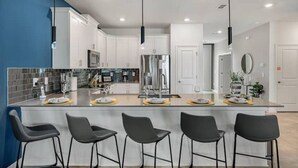 Une cuisine moderne avec des meubles blancs, un îlot central doté de tabourets de bar et des appareils électroménagers en acier inoxydable.