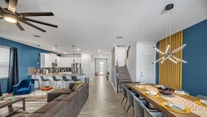 Une cuisine moderne dotée d’un îlot central, d’un coin repas avec une longue table et d’un escalier menant à un niveau supérieur.
