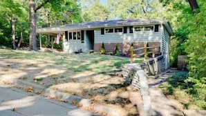 A single-story house with a front porch, a small deck, and a yard with trees and a stone wall. - The Manhattan Charm! (Manhattan)