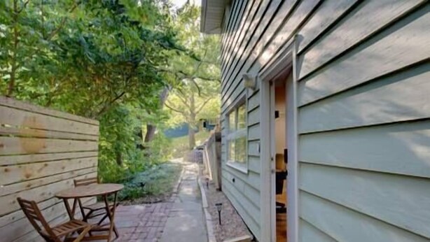 A wooden deck with a table and chairs, a pathway leading to a building with a door, and a wooden fence. - The Manhattan Charm! (Manhattan)