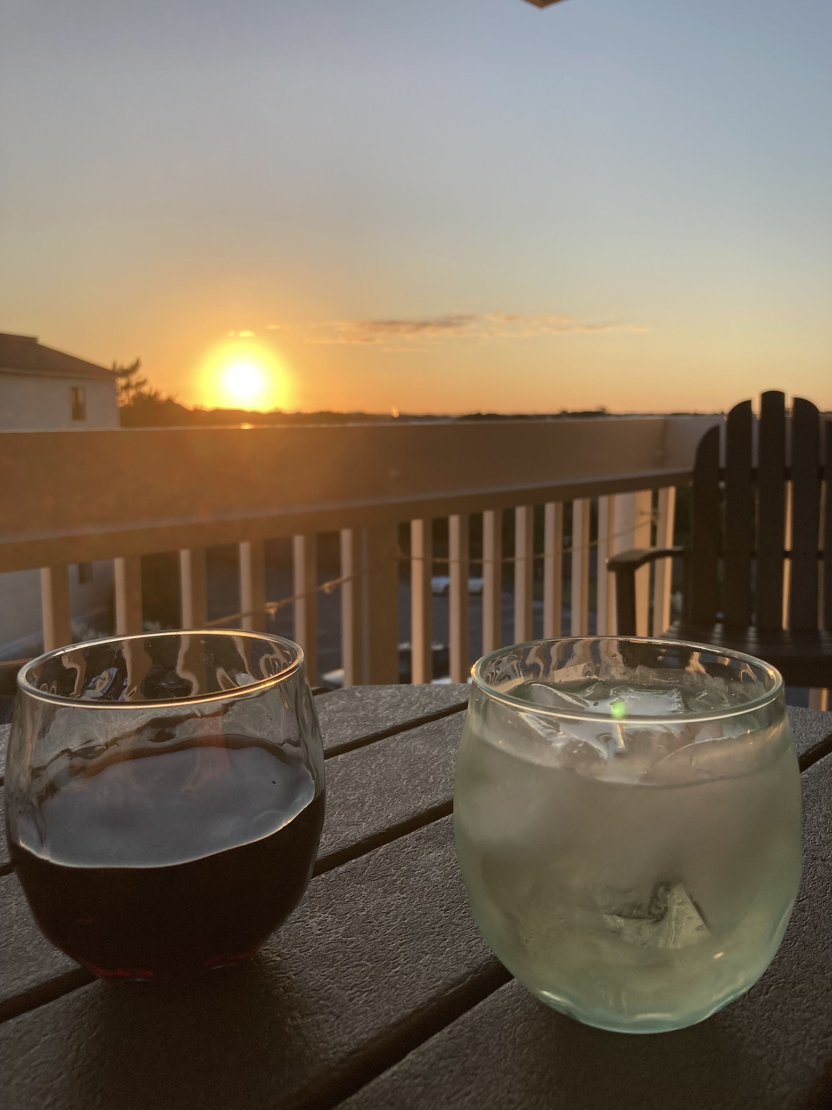 Two glasses on a wooden table with a sunset view in the background.
