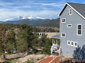 Une maison à deux étages avec un porche, une vue sur les montagnes et un ciel dégagé.