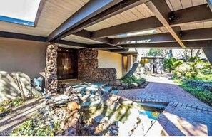 A covered outdoor area with a stone wall, a small water feature, and a paved walkway. - Mid Century Home on 5 Gated Acres by Oak Creek (Sedona)