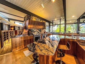 A modern kitchen with a large island, wooden cabinetry, and a stone backsplash. - Mid Century Home on 5 Gated Acres by Oak Creek (Sedona)