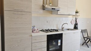 A modern kitchen with light wood cabinetry, a gas stove, a built-in oven, and a stainless steel range hood. - ROYAL HOUSE PALACE (Caserta)
