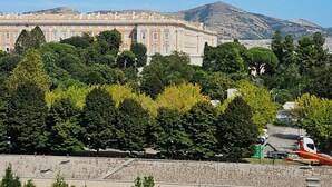 A large, historic building with classical architecture, surrounded by lush green trees and a clear blue sky. - ROYAL HOUSE PALACE (Caserta)