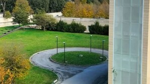A modern building with a glass facade, a landscaped area with a curved driveway, and a view of a hilly landscape in the background. - ROYAL HOUSE PALACE (Caserta)