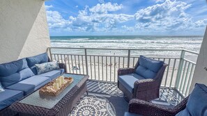 Ein Balkon mit Korbmöbeln, einem gemusterten Teppich und Blick auf Strand und Meer.