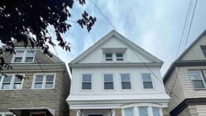 A two-story house with a front entrance, a blue door, and a white garage door. - Easy travel to NYC! Perfect house for family trips with Free parking  (Bayonne)