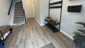 A hallway with a wooden floor, a staircase, a black metal rack, and a wall-mounted mail slot. - Easy travel to NYC! Perfect house for family trips with Free parking  (Bayonne)