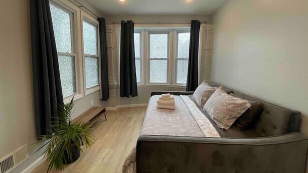 A room with a bed, a sofa, and large windows with curtains. - Easy travel to NYC! Perfect house for family trips with Free parking  (Bayonne)