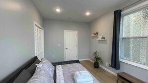 A bedroom with a bed, a door, a window, and a shelf with items. - Easy travel to NYC! Perfect house for family trips with Free parking  (Bayonne)