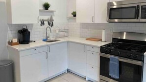 A modern kitchen with white cabinets, a stainless steel stove, a microwave, and a sink with a dish rack. - Easy travel to NYC! Perfect house for family trips with Free parking  (Bayonne)