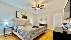 Ein Schlafzimmer mit Bett, Schreibtisch, Stuhl, Globus und Deckenventilator.