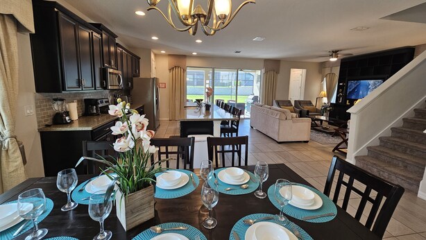 A dining area with a table set for four, a kitchen with dark cabinets, and a living area with a sofa and TV. - Solara Resort private POOL HOME 4 Bed (Kissimmee)