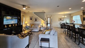 A spacious living room with a television, sofas, a coffee table, and a dining area with chairs and a table. - Solara Resort private POOL HOME 4 Bed (Kissimmee)