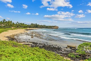 A beach with clear blue water, a rocky shoreline, and lush greenery. - Poipu Sands Beach Villa (Koloa)