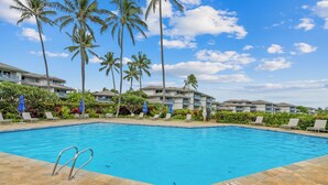 Ein Swimmingpool mit Liegestühlen und Palmen, umgeben von Hotelgebäuden.