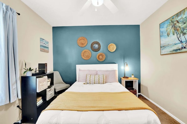 A bedroom with a bed, a desk, a chair, a desk lamp, and a painting on the wall.