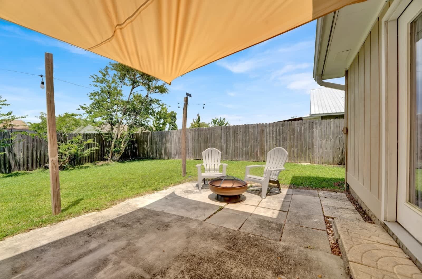 A patio with a fire pit, two Adirondack chairs, and a covered area.