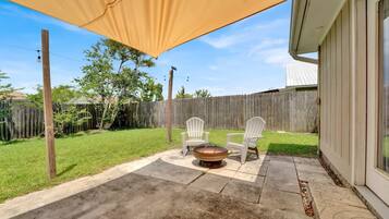 A patio with a fire pit, two Adirondack chairs, and a covered area.