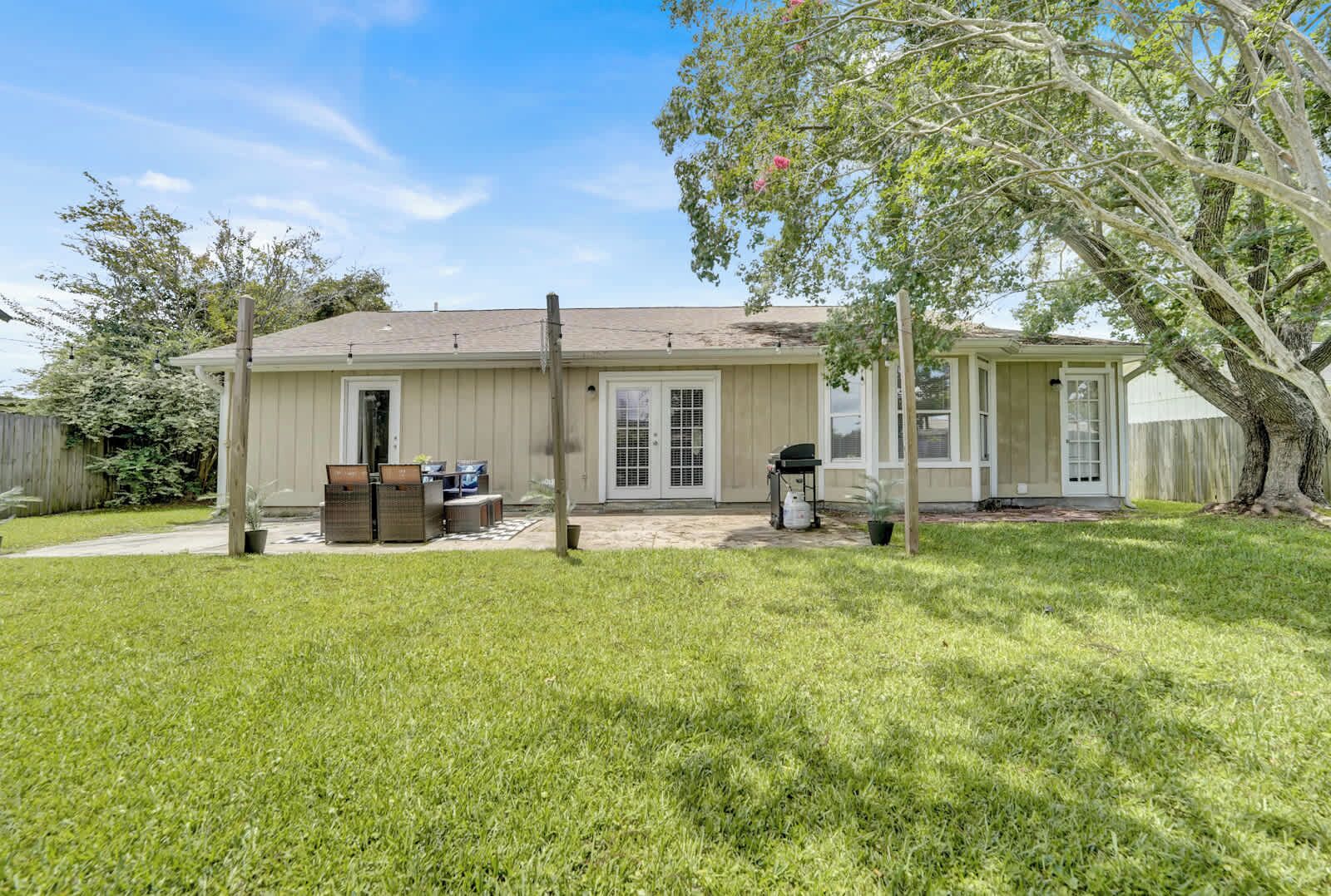 A single-story house with a covered patio, a fenced yard, and a large tree.