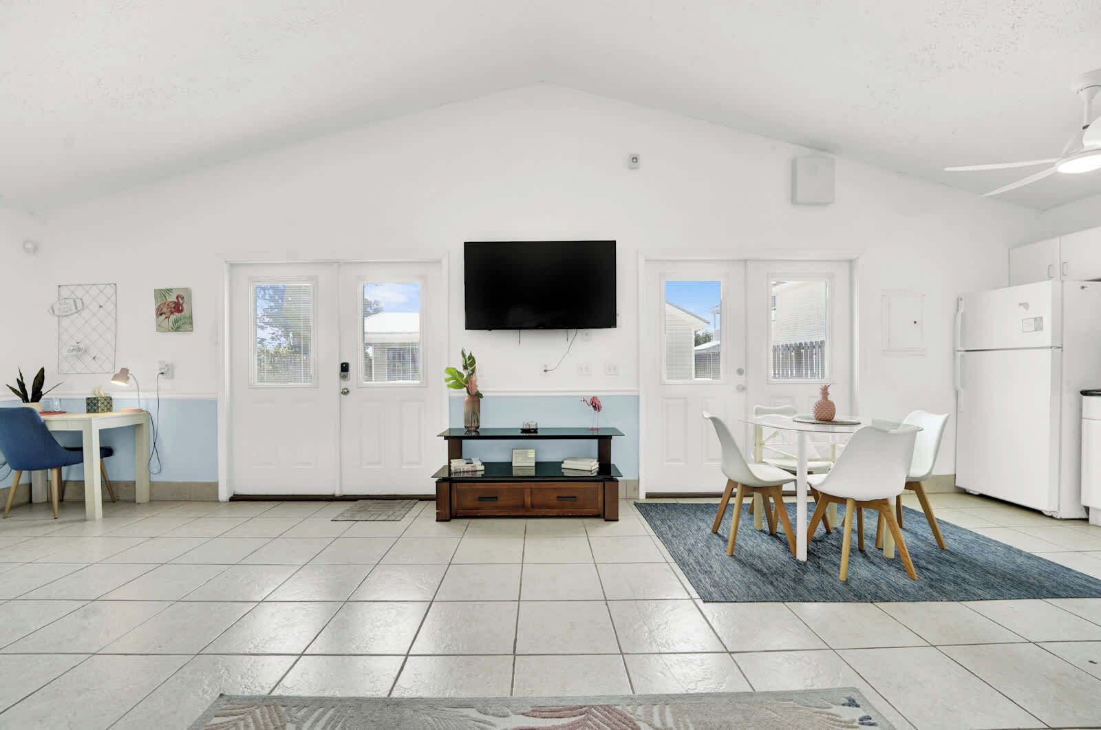 A spacious kitchen with white cabinets, a dining area with a table and chairs, and a TV mounted on the wall.