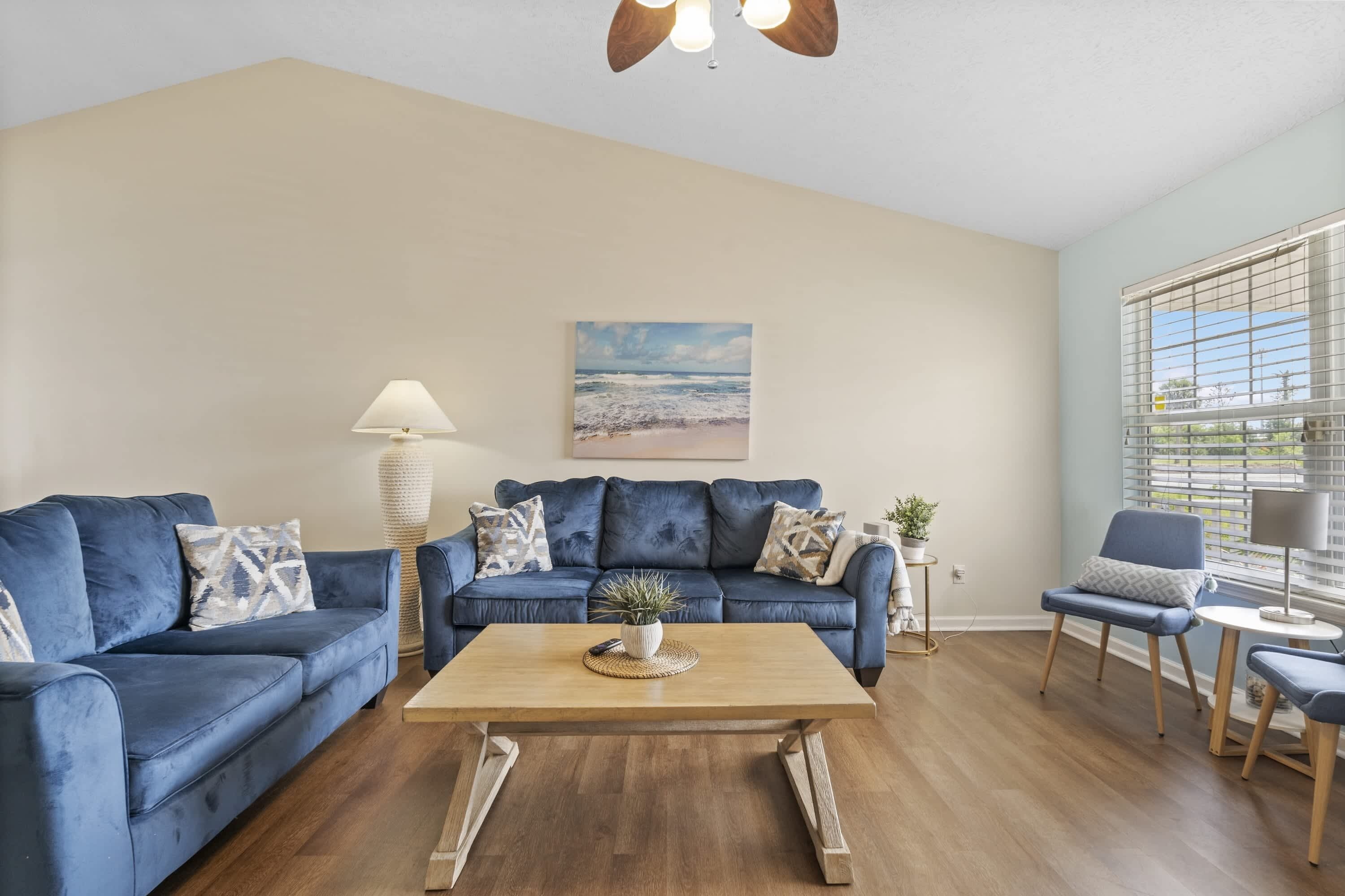 Ein Wohnzimmer mit blauem Sofagarnitur, einem Holztisch und einer Lampe.