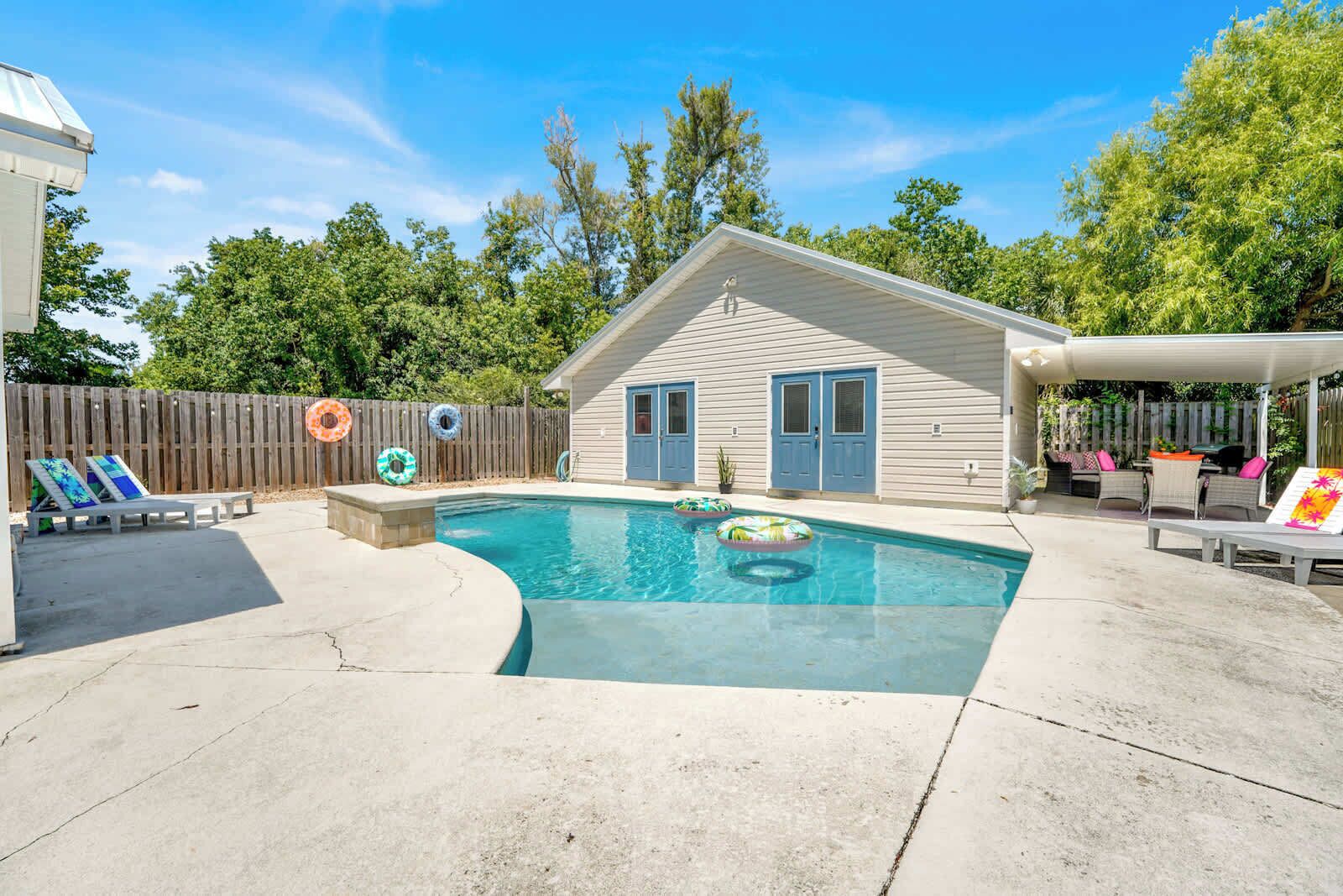 A backyard with a swimming pool, lounge chairs, and a wooden fence.