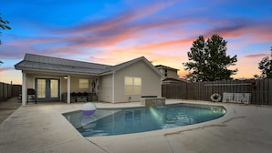 A residential backyard with a swimming pool, a wooden deck, and a house with a metal roof.