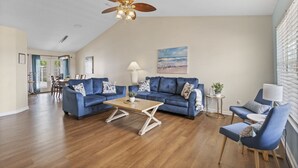 A spacious living room with a blue sofa set, a wooden coffee table, and a ceiling fan.