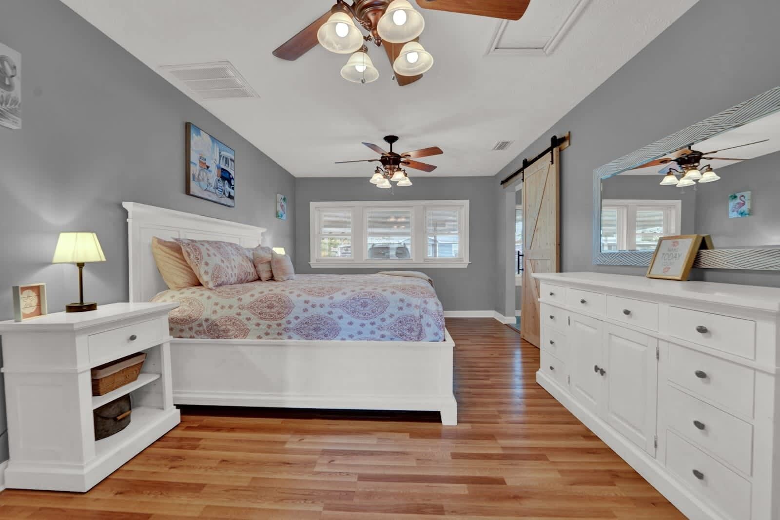 Une chambre à coucher comprenant un lit, des tables de chevet, une commode, un ventilateur de plafond et une fenêtre.
