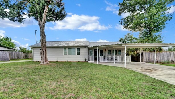 A single-story house with a covered patio, a fenced yard, and a large tree.