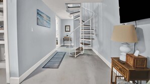 A modern interior with a spiral staircase, a wooden side table with a lamp, and a painting on the wall. - Adorable 1 BDR with Full Kitchen Deck Washer Dryer (Lynn Haven)