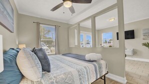 Un dormitorio con cama, ventilador de techo, ventana y vistas al exterior.