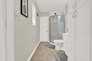 A narrow hallway leading to a bathroom with a toilet, shower, and a white door.