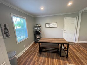 A dining area with a wooden table and bench, a coffee shelf, and a welcome sign on the wall.