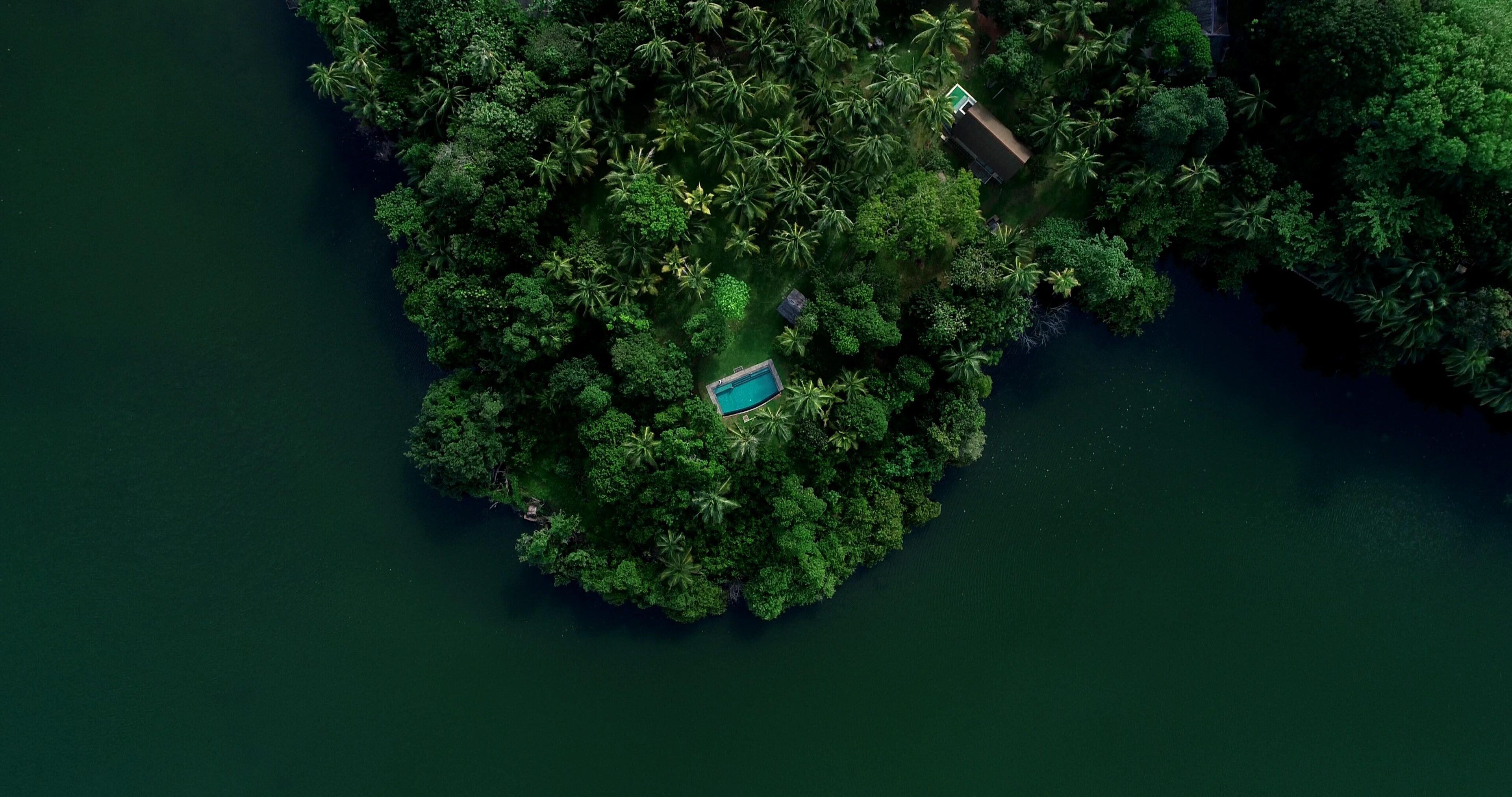 Vista aérea de una isla tropical con vegetación exuberante, una piscina y dos edificios.