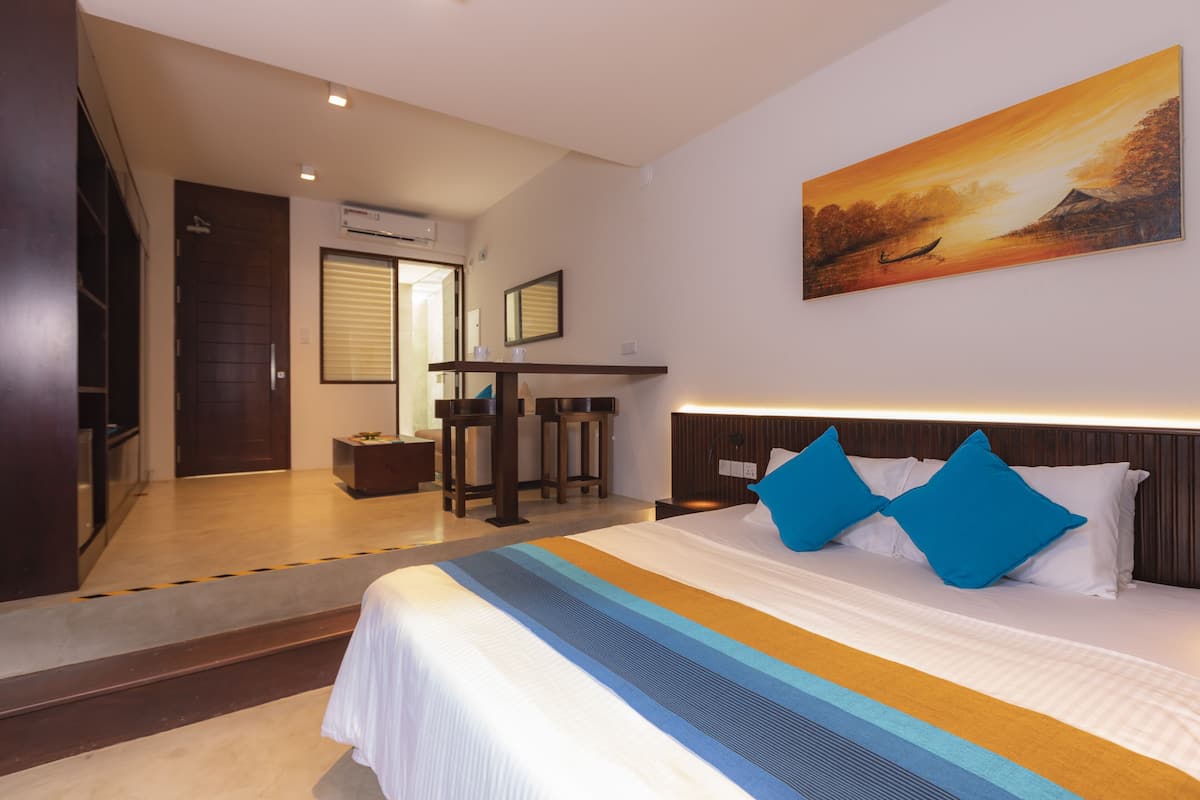 Une chambre d’hôtel avec un grand lit, un tableau au mur et un bureau avec des chaises.