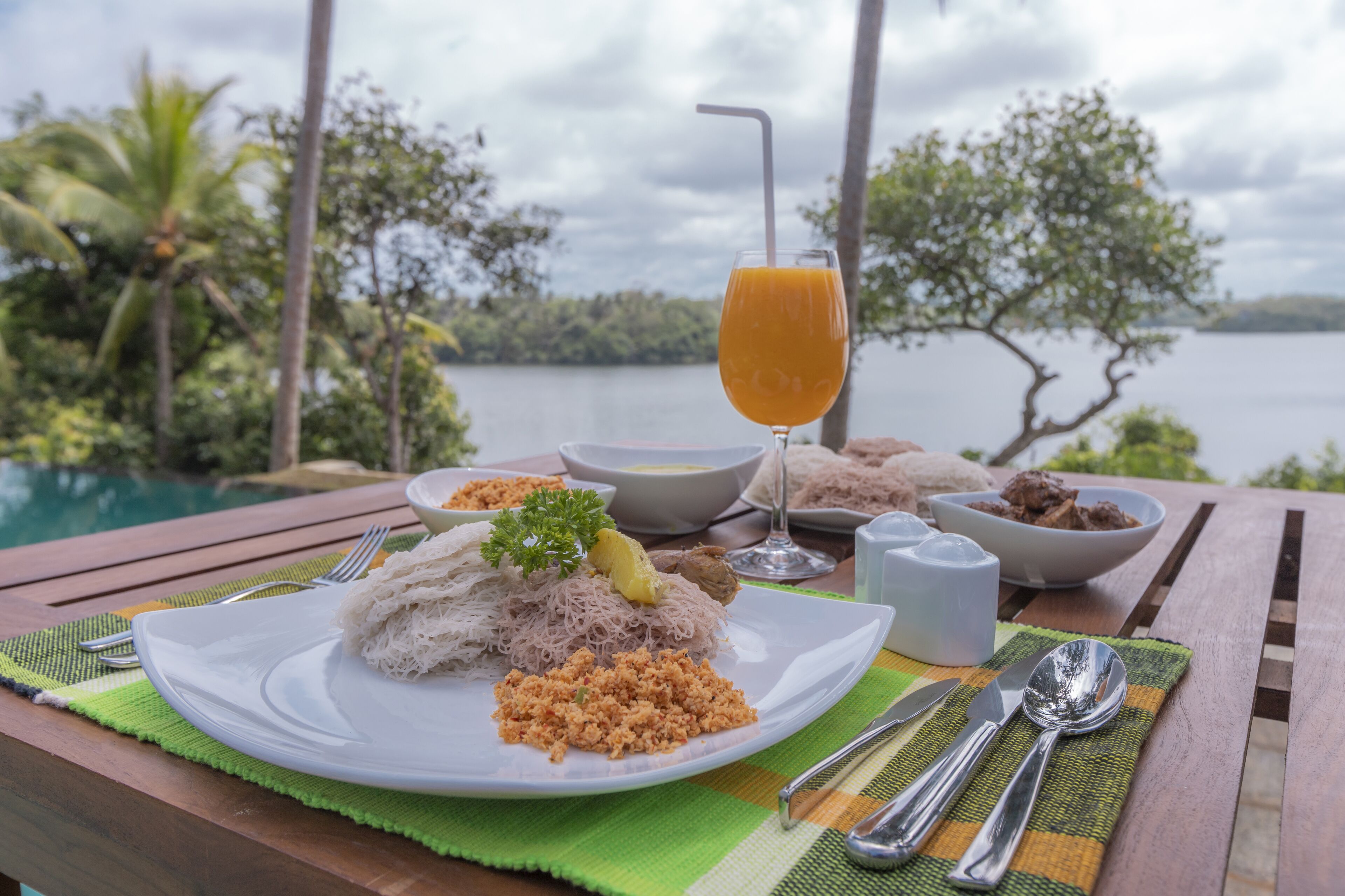 Una mesa de comedor con un plato de comida, un vaso de jugo de naranja y vistas a un lago y árboles.