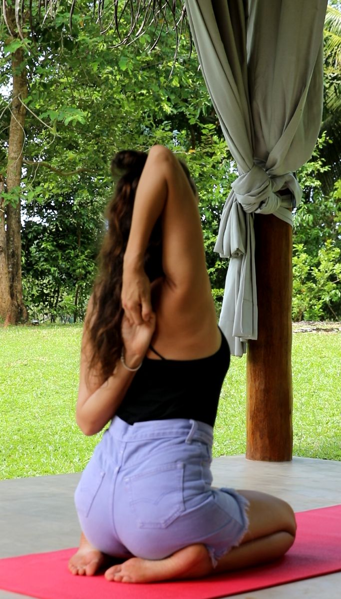 A person performing a yoga pose on a mat outdoors with trees and a gazebo in the background.
