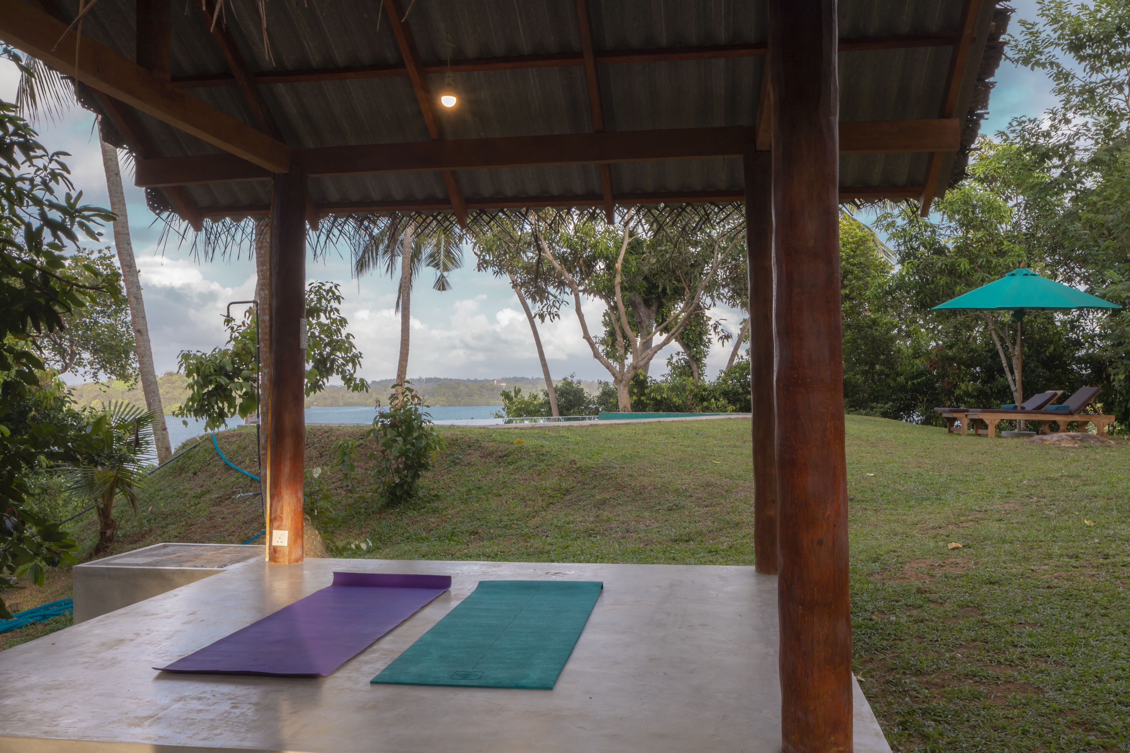 An outdoor covered area with exercise mats, a view of the sea, and a pool area with lounge chairs.