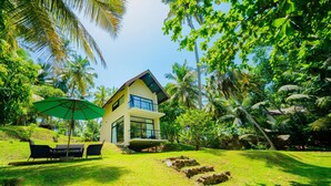 Une maison moderne dotée d’un balcon, entourée d’une végétation luxuriante et de palmiers.