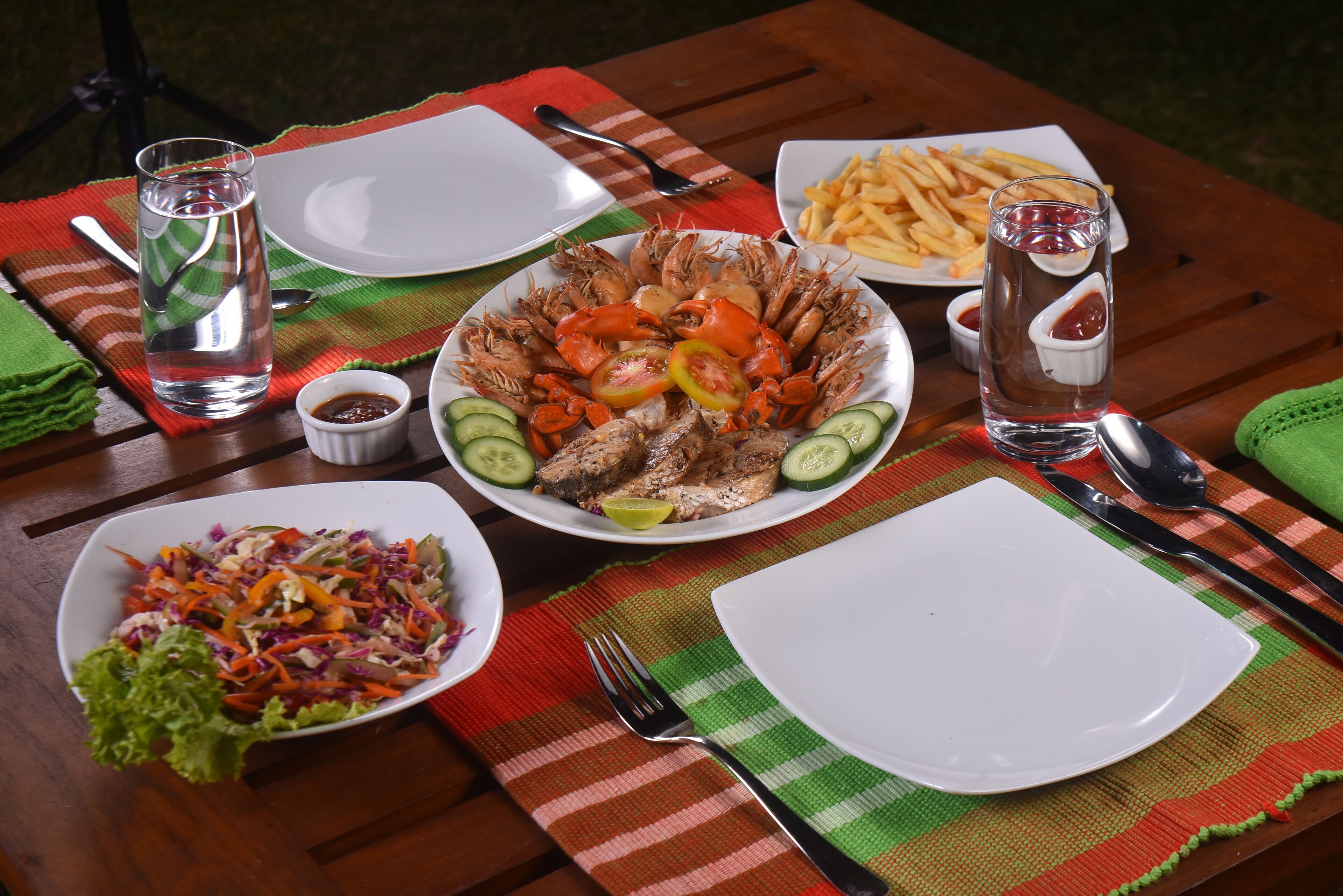 A table set with plates of food, including shrimp, salad, and fries, along with glasses of water and a fork.