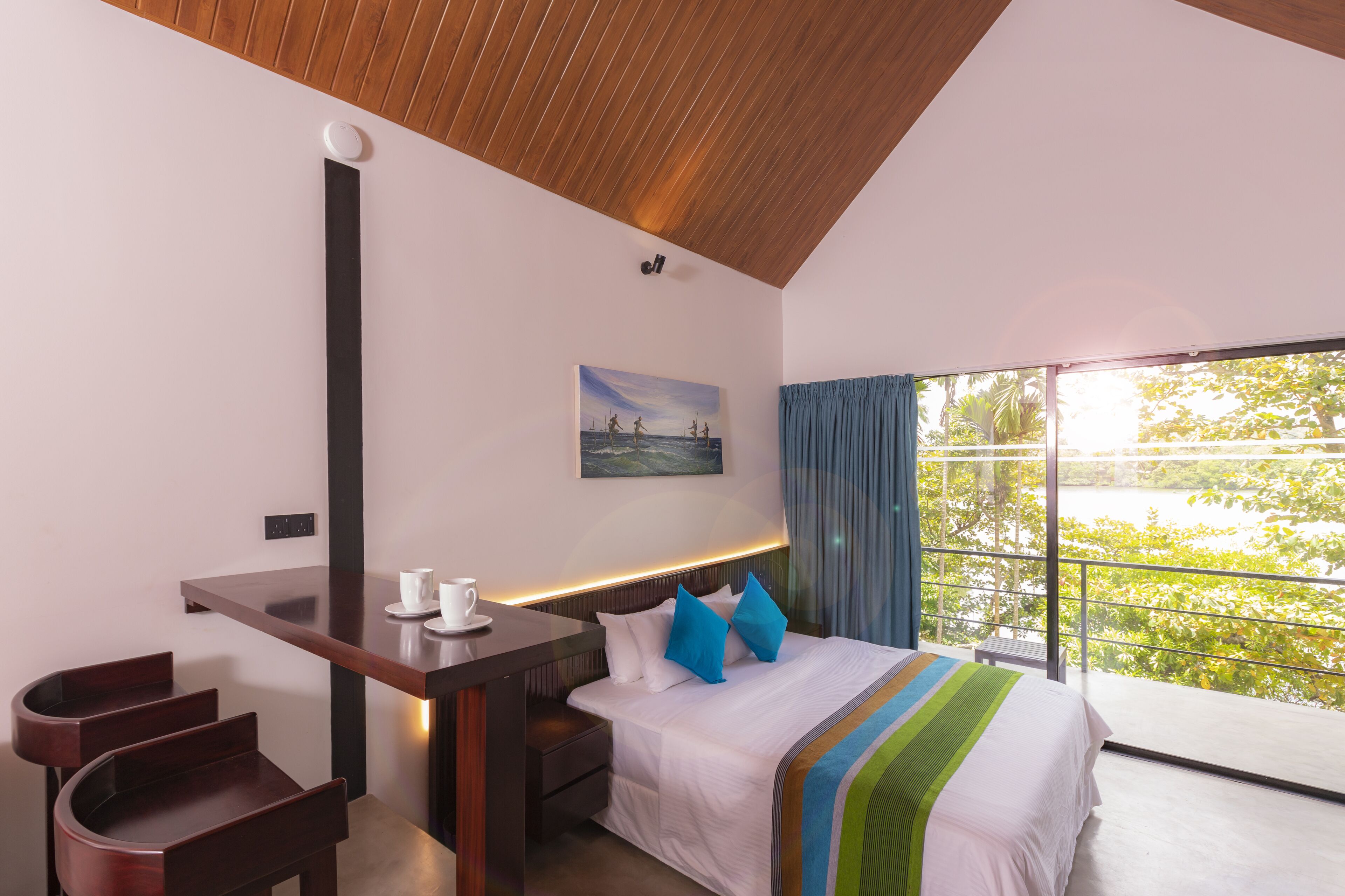 Ein modernes Hotelzimmer mit einem großen Bett, einem Schreibtisch mit Stuhl, Blick auf einen See und einem Gemälde an der Wand.