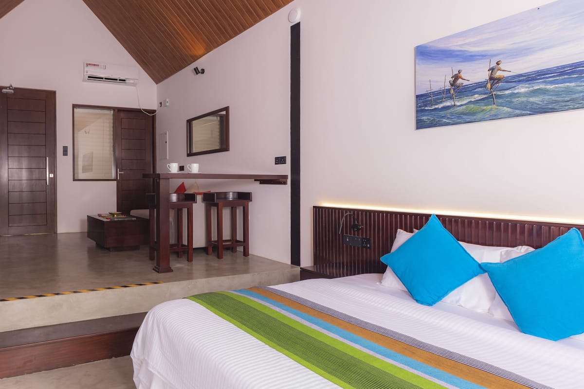 Une chambre d’hôtel avec un lit, un tableau représentant des surfeurs, un bureau et un miroir.
