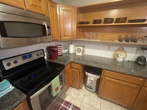 A kitchen with wooden cabinets, a stainless steel microwave, a black stove, a red coffee maker, and a trash can.