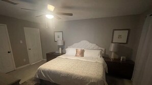 Une chambre à coucher avec un lit, des tables de chevet, un ventilateur de plafond et des tableaux encadrés accrochés aux murs.