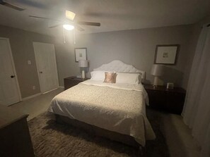 A bedroom with a bed, nightstands, a ceiling fan, and framed pictures on the walls.